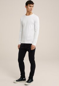 Camisa blanca de manga larga hecha de algodón, combinada con jeans negros ajustados y zapatillas verdes con suelas y detalles blancos.