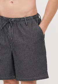 Pantalones cortos a rayas en blanco y negro fabricados con un tejido liviano, con cintura elástica, cordón y bolsillos laterales.