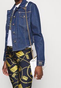 Blå denimjacka med silverdetaljer, fyra frampocket och långa ärmar. Kombinerad med svarta leggings med guld kedjemönster. Vit väska med kedjereim.