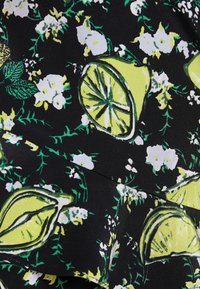 Svart tyg med ett blommönster med gröna blad och gula citroner. Designen innehåller vita blommor och använder djärva, starka färger.