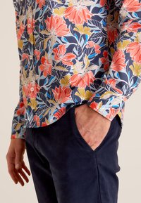 Korte mouwen bloemenoverhemd in marineblauw met levendige rode en gele bloemen. Voorzien van een knoopsluiting aan de voorkant, een gebogen zoom en een comfortabele pasvorm.