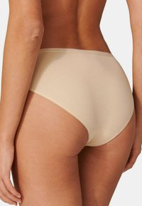 Beige puuvillapantit, venyvä kangas, saumaton muotoilu, kohtuullinen peittävyys, kankaan pinta sileä lievällä kiillolla, matala vyötärönauha.