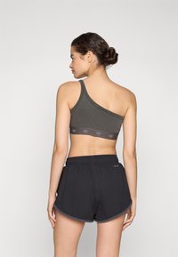 Grå ribbad sport-bh med en axelrem, utrustad med ett mörkt band med en logotyp. Matchas med svarta avslappnade shorts; shortsen har en fågeldetalj.