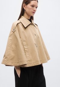 Bež kapa jakna s širokim ovratnikom, kopčanjem na gumbe, bočnim džepovima i ležernim krojem od teksturiranog tkanja.