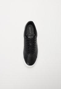 Adidași din piele neagră cu talpă din cauciuc albă, având vârf rotund, design cu șireturi și un logo pe limbă. Textură netedă.