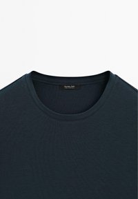 Námořnická modrá trička s jemnou ribovanou texturou, s kulatým výstřihem a malou černou nášivkou s nápisem "Massimo Dutti" uvnitř výstřihu.