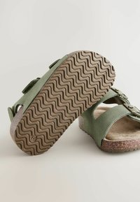 Gröna mockasandaler med två justerbara remmar, korkfotbädd och texturerad brun gummisula med ett zigzag-mönster.