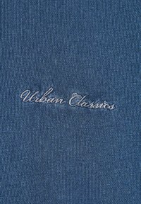 Tessuto blu con una trama a coste, caratterizzato dal testo ricamato "Urban Classics" in grigio chiaro. Design semplice senza ulteriori motivi.