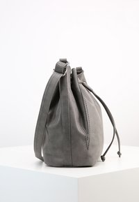 Grå ruskinds bucket bag med en struktureret form, justerbar rem og snørrelukning, der har tonal syning og en glat tekstur.
