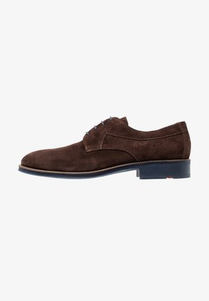 Chaussure habillée en daim marron avec un bout rond, des coutures minimalistes, des accents de lacets bleus et une semelle noire. Talon plat avec un détail de bord contrastant.