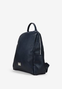 Mochila de cuero azul marino con una textura suave, forma redondeada, bolsillo lateral con cremallera y un pequeño acento metálico en la parte frontal.