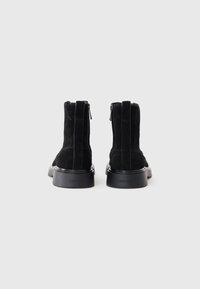 Black suede ankle boots with a smooth rubber sole. Features a side zipper and embossed logo on the back. Rounded toe and minimal design.