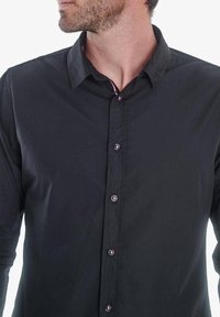 Camisa negra de botonadura frontal con un cuello clásico, mangas largas y acentos de botones en contraste, confeccionada en una tela suave y ligera.