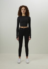 Svart kortärmad topp med slät textur; kombinerad med högmidjade, figurnära svarta jeans; vita sneakers fulländar outfiten.