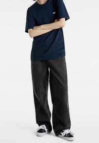 Marineblauwe t-shirt met korte mouwen en een klein wit logo, gecombineerd met losse zwarte broeken en zwart-witte sneakers. Eenvoudig en casual ontwerp.