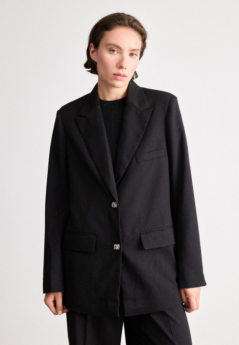 Sacou negru cu un finisaj ușor texturat, având două buzunare frontale și nasturi decorativi. Formă ajustată cu rever înclinat.