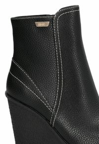 Botine negre cu toc wedge, fabricate din piele texturată. Prezintă cusături albe și o mică placă logo metalică în partea de sus.