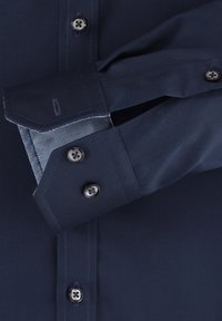 Donkerblauwe langemouwshirt met een gestructureerde kraag, knoopsluiting aan de voorkant, contrasterende binnenmanchetten in een klein ruitpatroon en metalen knopen.