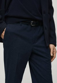 Pantaloni testurizzati blu navy realizzati in tessuto intrecciato, con cintura in pelle nera e tasche laterali, abbinati a un top in maglia.