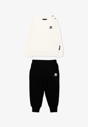 Wit shirt met lange mouwen met schouderknopen en zwart "JR" logo, gecombineerd met zwarte broek met elastische taille en wit "JR" logo.