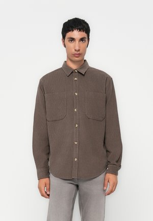 Chemise en velours côtelé marron avec boutons à l'avant, manches longues et deux poches poitrine. Elle présente un col classique et un tissu texturé.