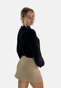 Zwarte blouse met lange mouwen van een gestructureerde stof, gecombineerd met een korte beige suède rok. De outfit heeft een eenvoudig ontwerp met een kraagloze halslijn.