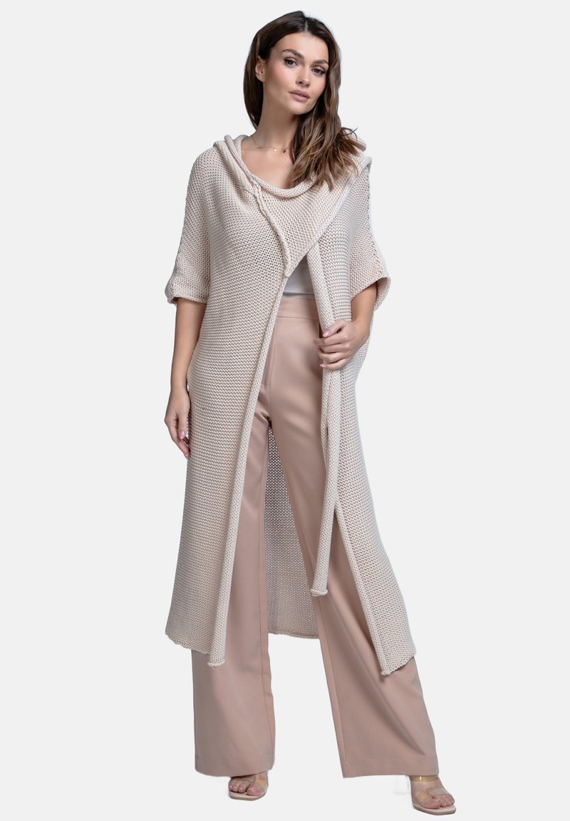 Beżowy sweter z dzianiny z kapturem, otwarty z przodu, z krótkimi rękawami, połączony z jasnoróżowymi spodniami o szerokich nogawkach. Miękka tekstura, casualowy design.