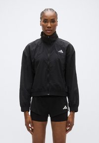 Must tuulekindel jope, millel on kõrge krae ja lukuga sulgur, elastsed mansetid ja alläär; sisaldab valgeid Adidas logo detaile.