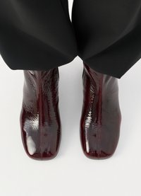 Burgundowe klasyczne skórzane botki za kostkę o błyszczącej powierzchni, z efektownym designem i spiczastym noskiem. Szczegół szwu biegnie wzdłuż boku.