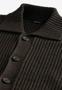 Cardigan marron côtelé avec un col rabattable, comportant quatre gros boutons et une texture douce, étiqueté "NEXT."