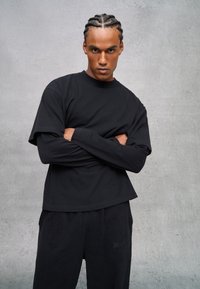Schwarzes übergroßes T-Shirt aus Baumwolle mit kurzen Ärmeln und rundem Ausschnitt, kombiniert mit schwarzen Hosen mit dezenten gestickten Details.