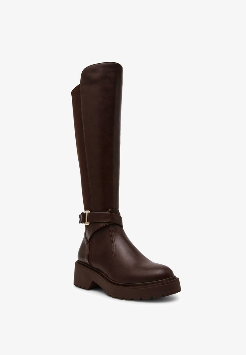 Bota marrón de cuero hasta la rodilla con punta redondeada, suela gruesa, correa en el tobillo con herrajes dorados y textura superior lisa.