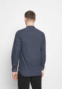Camicia a maniche lunghe blu navy con motivo geometrico bianco. Presenta polsini con bottone, orlo curvo e colletto. Realizzata in un tessuto liscio.