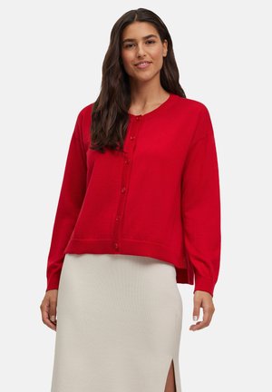 Rode gebreide cardigan met een ronde halslijn, lange mouwen en sluiting met vijf knopen, gecombineerd met een crèmekleurige rok met een zijsplit.