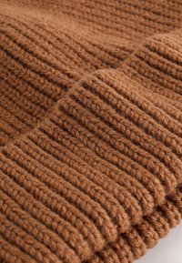 Bruin gebreide stof met een dikke, geribbelde textuur. Het garen lijkt zacht en grof, met een warme, aardse tint.