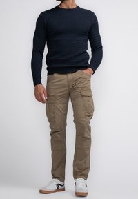 Tmavě modrý svetr z texturovaného úpletu, béžové cargo kalhoty s více kapsami a bílé tenisky s černými detaily.