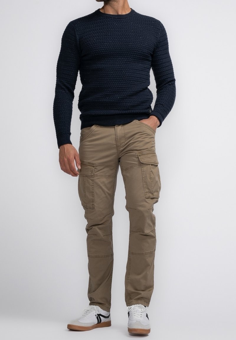 Tmavě modrý svetr z texturovaného úpletu, béžové cargo kalhoty s více kapsami a bílé tenisky s černými detaily.