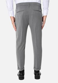 Pantaloni grigi su misura con una texture liscia, due tasche posteriori e orli arrotolati. Abbinati a scarpe nere lucide, visti da dietro.