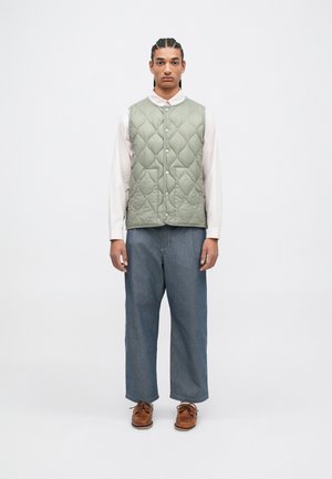 Rūpīgi izšūts, gaiši zaļš veste ar pogu aizdari, valkāta pār rozā krekli. Kombinēta ar brīviem ziliem džinsu biksēm un brūnām kurpēm.