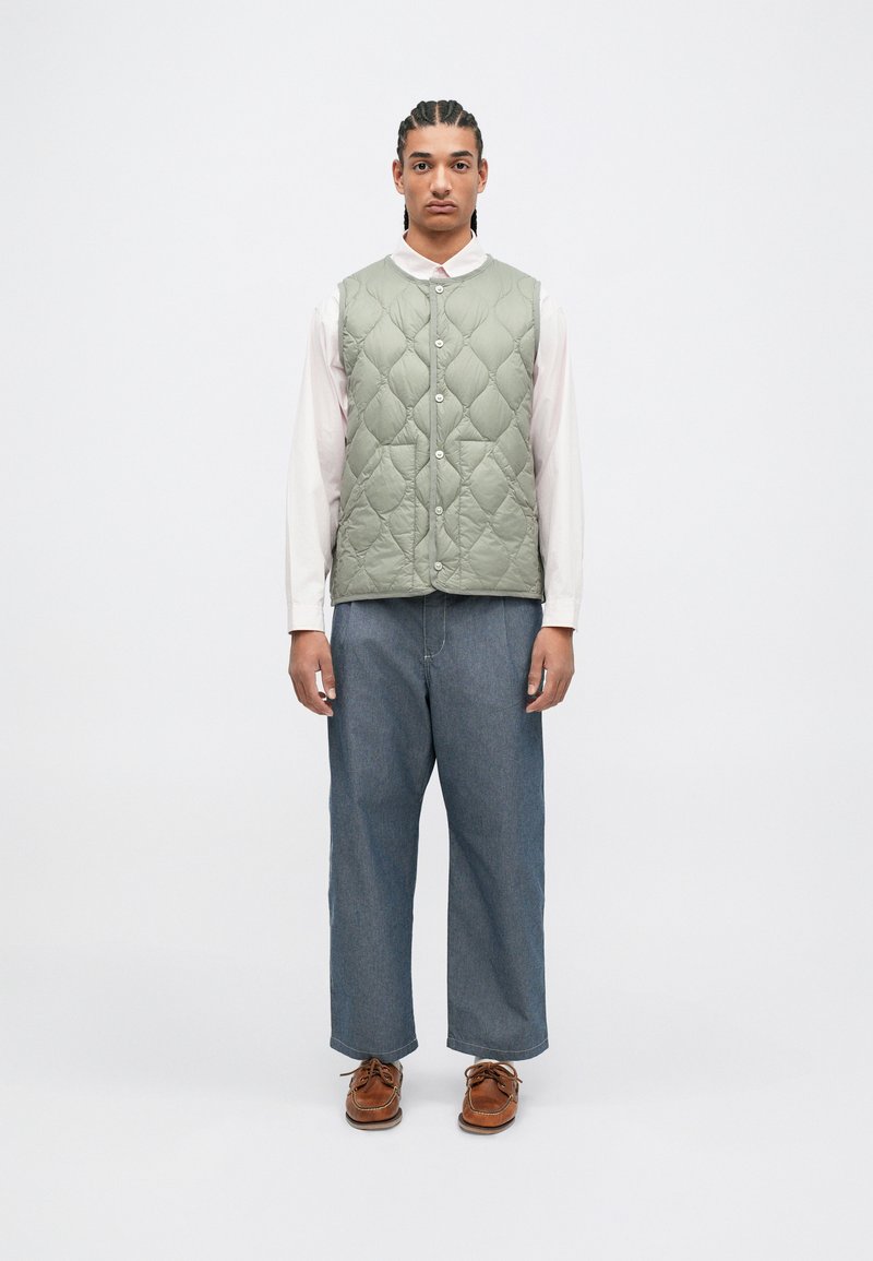 Rūpīgi izšūts, gaiši zaļš veste ar pogu aizdari, valkāta pār rozā krekli. Kombinēta ar brīviem ziliem džinsu biksēm un brūnām kurpēm.