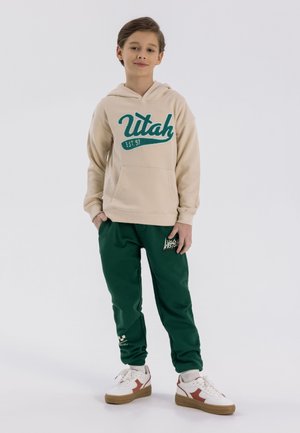 Beige kapucnis pulcsi "Utah" grafikával türkiz színben; zöld göncök logóval; fehér sneaker piros kiegészítőkkel; laza fazon.