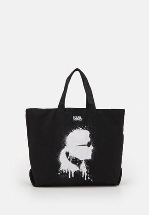Sort tote-taske med korte håndtag med et hvidt spraymaling-stil grafik af et ansigt med solbriller og teksten "Karl Lagerfeld."