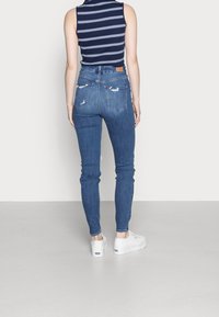 Smala blå jeans gjorda av denim med slitna detaljer. Kombinerat med en åtsittande randig ärmlös topp och vita sneakers.