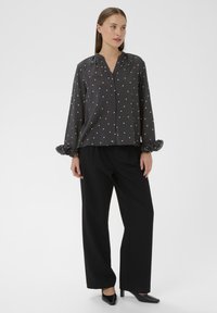 Grå skjorte med hvide prikker, afslappet pasform og flæser på manchetterne. Sammen med sorte brede bukser og stilfulde sorte sko.