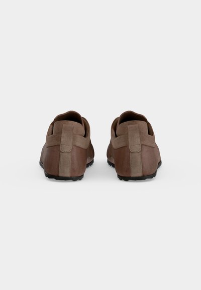 Paire de chaussures en cuir marron à enfiler, montrée de dos sur un fond gris clair uni.