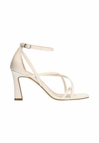 Beige hoge hakken sandaal met een open teen, dunne kruislingse banden en een enkelbandje. De hak is ongeveer 7,5 cm hoog.