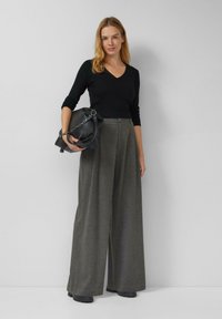 Czarny prążkowany top na długi rękaw z dekoltem w serek połączony z szarymi, wysokim stanem i szerokimi nogawkami spodniami. Modelka trzyma czarną torebkę z detalem w postaci łańcuszka.