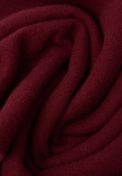Tecido bordô, macio e texturizado, drapeado em dobras suaves, exibindo um acabamento fino e felpudo com uma cor rica e profunda.