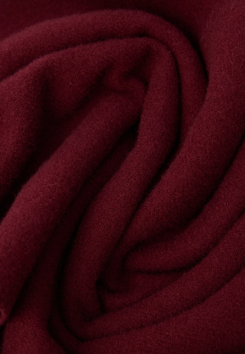 Burgunderrødt stof, blødt og tekstureret, draperet i glatte folder, der fremviser en fin, blød overflade med en rig, dyb farve.