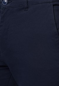 Blisko ujęcie granatowego materiału spodni, z gładką teksturą, płaską powierzchnią i kontrastowym szwem wzdłuż szwów i kieszeni.